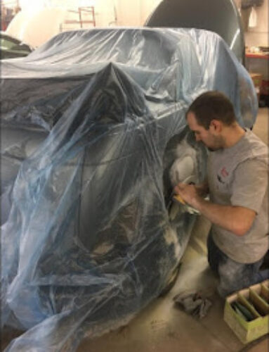 Man working with an automobile under plastic.